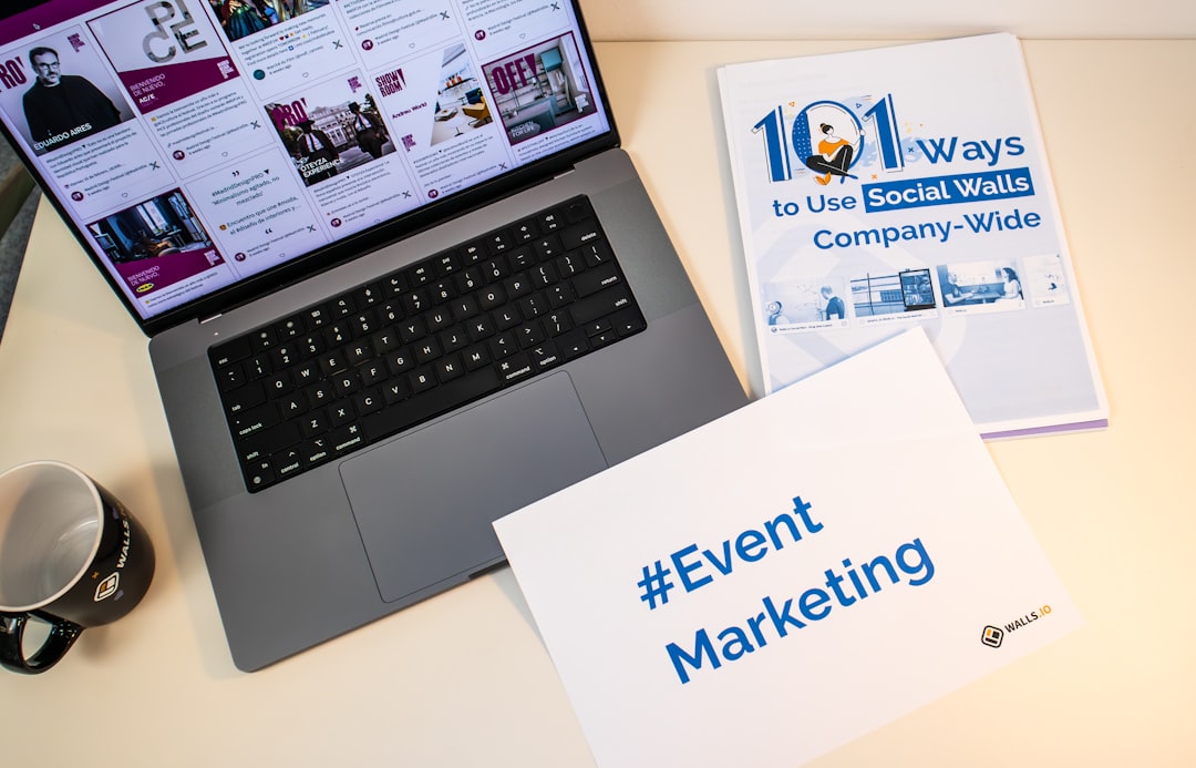 A desk with documents, a piece of paper with the hashtag #EventMarketing and a laptop showing a social media wall